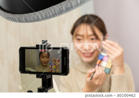 A woman shooting a make-up video on her smartphone 80100462