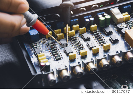 Technician checking ic on circuit board with multimeter probe 80117077