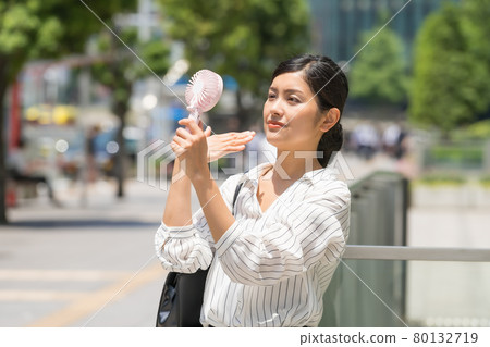 Mini fan in the business district (business woman with a handy fan) Mini fan in the business district (business woman with a handy fan) 80132719
