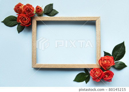 Flowers composition. Wooden frame and red roses and leaves on blue background Flowers composition. Wooden frame and red roses and leaves on blue background 80145215