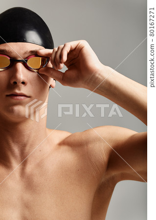 Young male swimmer preparing for the start, close-up portrait of a swimmer in a mask and a hat, gray background, copy space, swimming concept. Young male swimmer preparing for the start, close-up portrait of a swimmer in a mask and a hat, gray background, copy space, swimming concept. 80167271