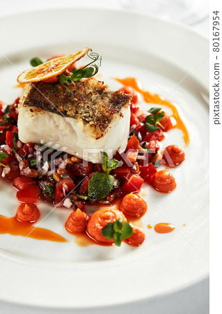 Black cod with vegetables, an appetizing piece of grilled black cod garnished with stewed vegetables on a white plate Black cod with vegetables, an appetizing piece of grilled black cod garnished with stewed vegetables on a white plate 80167954