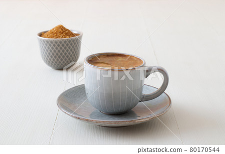 Cup of coffee on white wooden table with bowl of sugar cane. Low angle, closeup view. Cup of coffee on white wooden table with bowl of sugar cane. Low angle, closeup view. 80170544