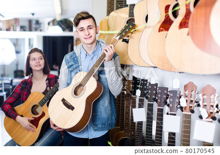 teenage customers deciding on suitable acoustic guitar in guitar shop teenage customers deciding on suitable acoustic guitar in guitar shop 80170545