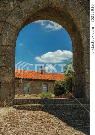 Stone house seen through wall gate arch 80232930