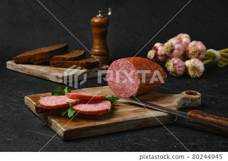 Smoked salami and sandwich on cutting board over black background 80244945