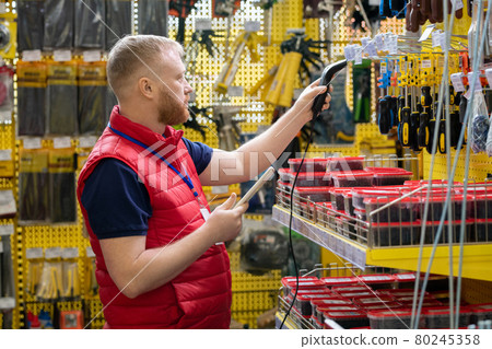 Young man with tablet and scanner checking prices of goods 80245358