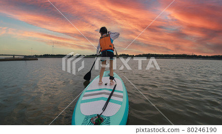 一個可愛的孩子在夏天的海裡玩 SUP 板和美麗的日落風景 80246190