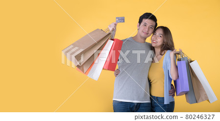 Asian couple holding credit card and shopping bags isolated on yellow background 80246327