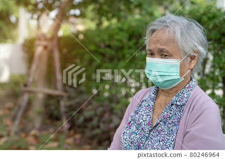 Asian senior or elderly old lady woman wearing a face mask sitting in park at home for protect safety infection Covid-19 Coronavirus. 80246964