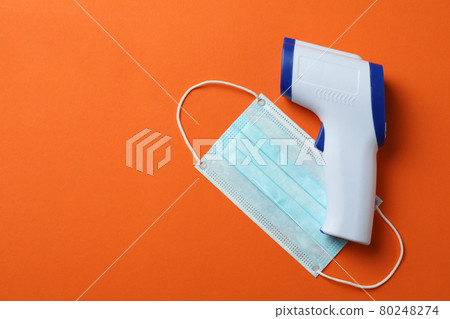 Thermometer gun and medical mask on orange background Thermometer gun and medical mask on orange background 80248274