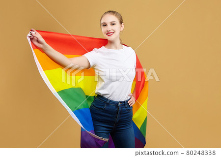 attractive blonde made posing with a rainbow LGBT flag. photo shoot in the studio on a yellow background attractive blonde made posing with a rainbow LGBT flag. photo shoot in the studio on a yellow background 80248338