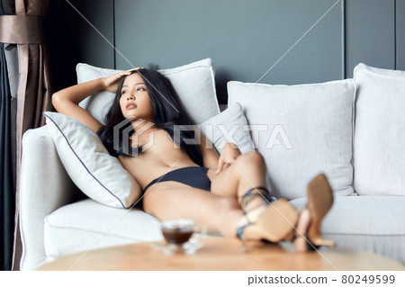 Asian topless girl lying on sofa with legs on the table with cup of coffee. shallow depth of field Asian topless girl lying on sofa with legs on the table with cup of coffee. shallow depth of field 80249599