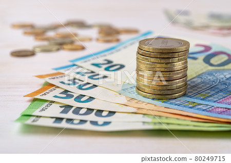 Stack of coins on euro paper banknotes in a fan shape over desk.  80249715