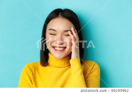 Beauty and makeup concept. Close up of beautiful asian woman laughing and looking flushed from compliments, standing over blue background 80249962