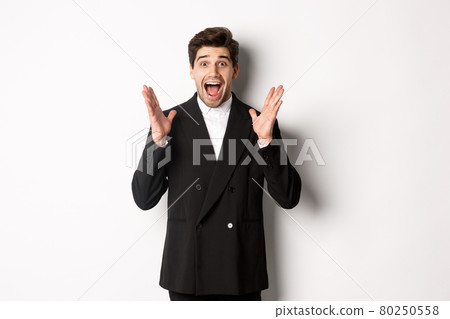 Portrait of surprised handsome businessman in suit, reacting to holidays promo, looking amazed at camera, standing over white background 80250558
