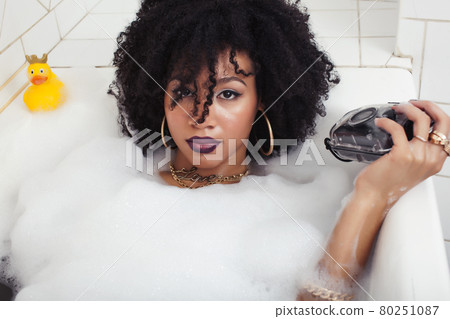 young afro-american teen girl laying in bath with foam, wearing swag jewelry flawless, making selfie young afro-american teen girl laying in bath with foam, wearing swag jewelry flawless, making selfie 80251087