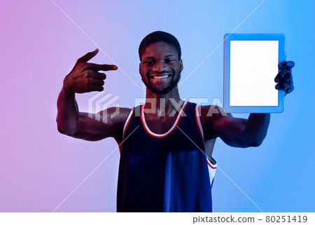 Positive black sportsman showing tablet pc with empty screen in neon light, mockup for app or website design 80251419