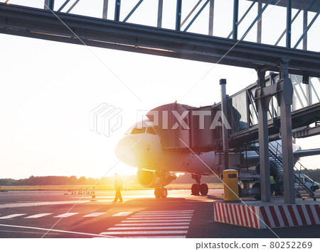 Airplane with terminal gangway of the airport building on sunset. Maintenance before the flight 80252269