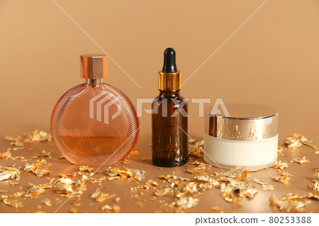 Moisturizer cream in glass jar, Serum in glass bottle with dropper pipette, perfume spray bottle and pieces of gold paper on golden background. Cosmetic set. Moisturizer cream in glass jar, Serum in glass bottle with dropper pipette, perfume spray bottle and pieces of gold paper on golden background. Cosmetic set. 80253388