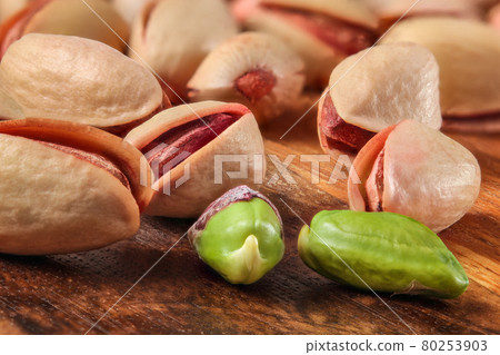 Pile of red Turkish pistachios on wooden board. Two of them peeled, green nut visible. Pile of red Turkish pistachios on wooden board. Two of them peeled, green nut visible. 80253903