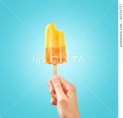 Bitten red frozen fruit ice cream popsicle in woman hand on blue background 80254757