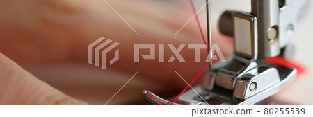 Hands pulling red thread in sewing machine needle 80255539