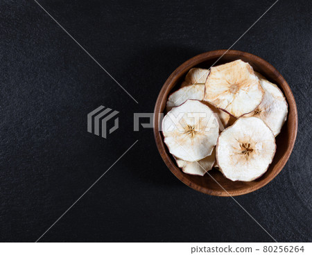 Dried Apple chips in a wooden bowl on a black stone background. Organic natural food. Dried Apple chips in a wooden bowl on a black stone background. Organic natural food. 80256264