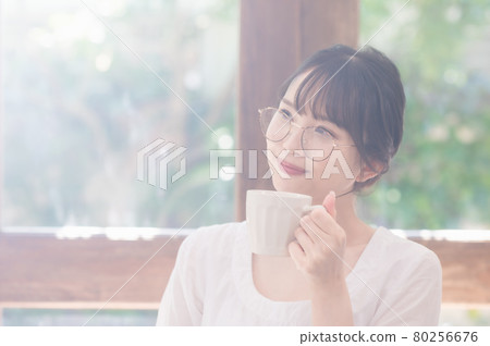 Young woman with glasses drinking coffee in the living room Young woman with glasses drinking coffee in the living room 80256676