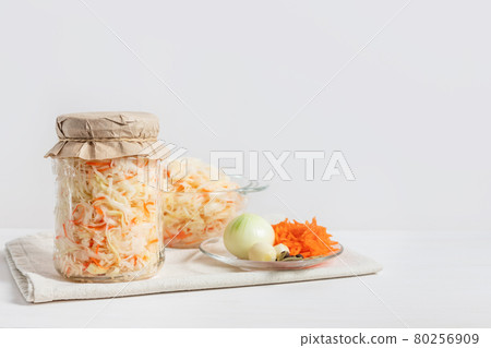 Homemade sauerkraut with carrots in a glass jar and bowl on a white wooden background. Fermented food. Homemade sauerkraut with carrots in a glass jar and bowl on a white wooden background. Fermented food. 80256909
