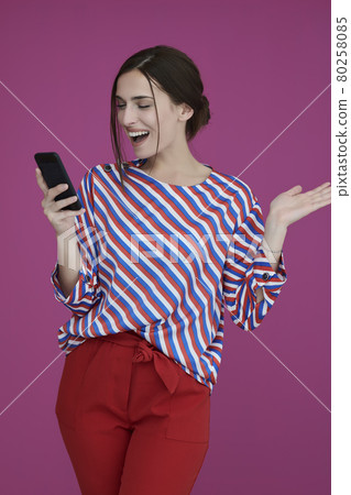 Portrait of young girl with happy face while using smartphone isolated on pink background 80258085