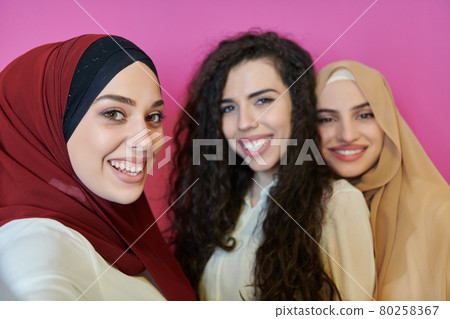 Muslim women taking selfie by mobile phone isolated on pink background Muslim women taking selfie by mobile phone isolated on pink background 80258367