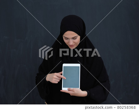 Young Arab businesswoman in traditional clothes or abaya and glasses showing tablet computer display Young Arab businesswoman in traditional clothes or abaya and glasses showing tablet computer display 80258368