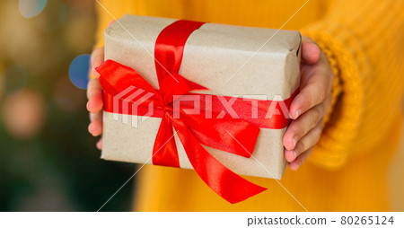 Woman in cozy yellow knitted sweater giving christmas craft gift boxes with red ribbon. Giving presents concept.Valentine day and mothers day gift concept 80265124