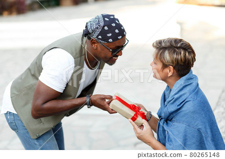 Happy middle age interracial couple sitting . Man giving Valentine's day gift to his woman,girlfriend or wife. Happy middle age interracial couple sitting . Man giving Valentine's day gift to his woman,girlfriend or wife. 80265148
