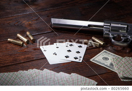 Gambling in cards, poker or blackjack for money. On a wooden table are a pistol with cartridges, cash dollars, and a deck of playing cards with an ACE of spades and a six. Dangerous gambling debts 80265660