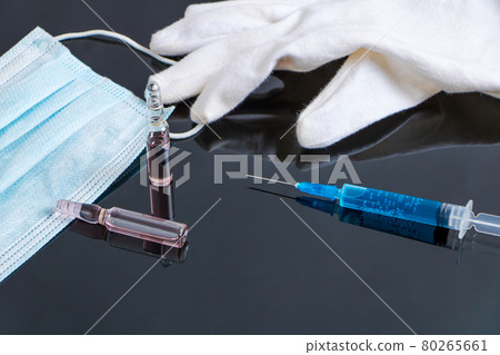 A medical mask, a syringe with the drug, ampoules with the drug and a medical white glove lie on a black table. 80265661