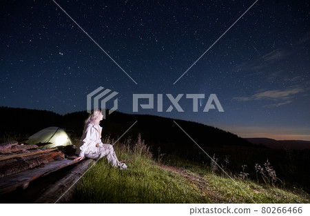 Young woman sitting near tent in mountains. 80266466