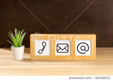 Contact us icons in modern wooden frame on desk. Brown textured wall. Copy space 80268922