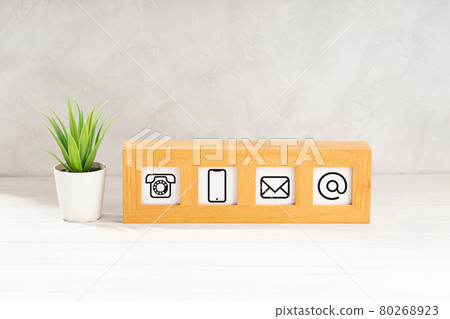 Contact us icons in modern wooden frame on desk. White textured wall. Copy space 80268923