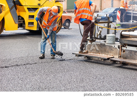 A team of road workers is laying fresh asphalt with industrial road machinery. A team of road workers is laying fresh asphalt with industrial road machinery. 80269585