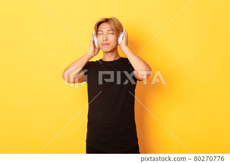 Relaxed and pleased handsome asian guy close eyes from satisfaction while listening music in wireless headphones, standing yellow background Relaxed and pleased handsome asian guy close eyes from satisfaction while listening music in wireless headphones, standing yellow background 80270776