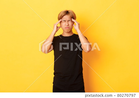 Portrait of troubled asian male student having headache, grimacing from pain and touching head, suffering migraine Portrait of troubled asian male student having headache, grimacing from pain and touching head, suffering migraine 80270797