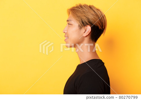 Profile of stylish handsome asian guy with fair hair looking left and smiling, standing over yellow background Profile of stylish handsome asian guy with fair hair looking left and smiling, standing over yellow background 80270799