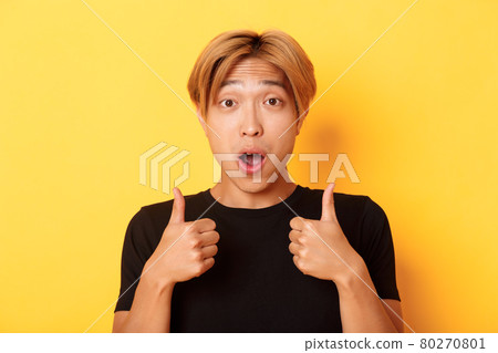 Close-up of impressed and excited handsome asian guy showing thumbs-up and looking amazed, standing over yellow background Close-up of impressed and excited handsome asian guy showing thumbs-up and looking amazed, standing over yellow background 80270801