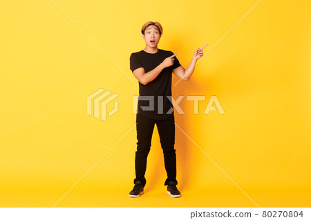 Full-length of amazed and impressed attractive asian guy pointing fingers upper right corner, showing logo, yellow background Full-length of amazed and impressed attractive asian guy pointing fingers upper right corner, showing logo, yellow background 80270804