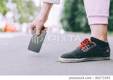 Young woman picks up from the asphalt fallen not crashed smartphone. Young woman picks up from the asphalt fallen not crashed smartphone. 80271895