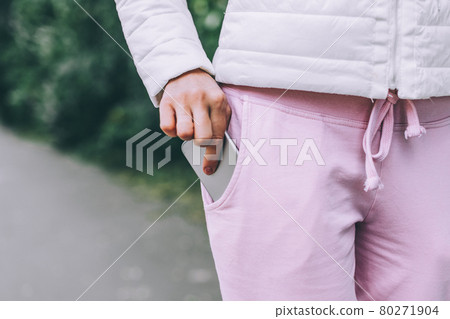 Woman's hand put smartphone in not zippered pocket on pants. Danger of dropping. 80271904