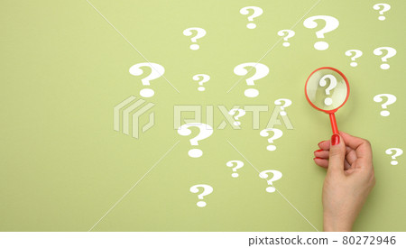 female hand holds a plastic magnifying glass and question marks on a green background. The concept of finding an answer to questions female hand holds a plastic magnifying glass and question marks on a green background. The concept of finding an answer to questions 80272946