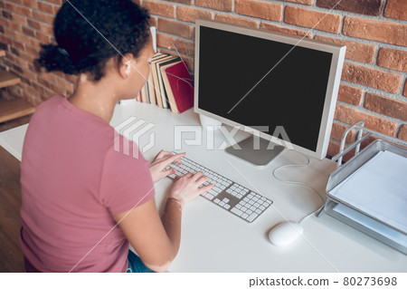 Young african american woman sitting at the table at her working place and looking busy Young african american woman sitting at the table at her working place and looking busy 80273698